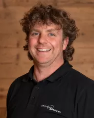 Mitarbeiterportrait / Foto mit braunem T-Shirt oder schwarzem Polo Shirt mit Zimmerei Hirschi Logo. Strahlend und lachend nach oben schauend oder direkt in die Kamera.