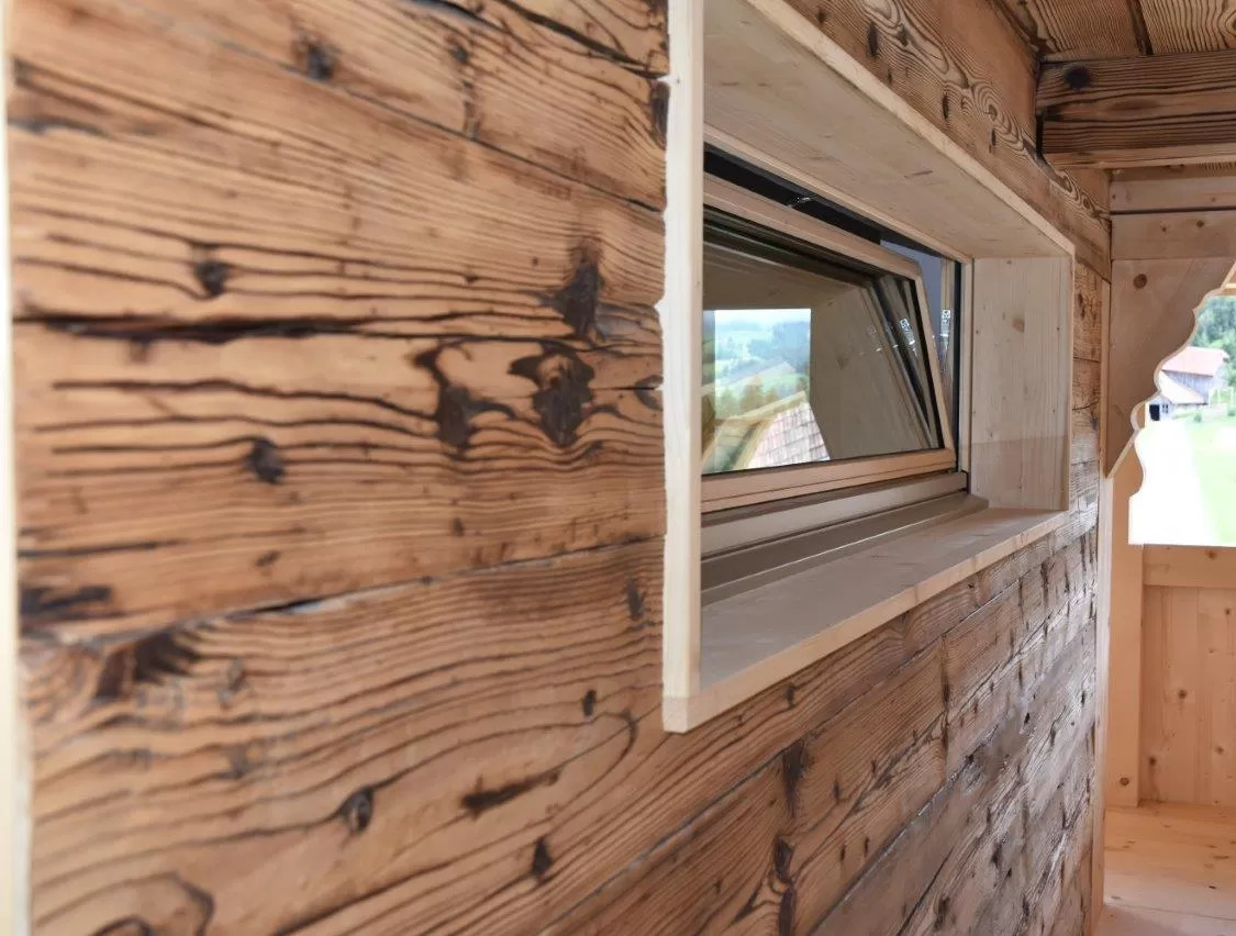Altes Bauernhaus von aussen ein liegendes, längliches Fenster integriert. die alte Wand ist ersichtlich. Rund herum steht ein neuer Fensterrahmen.