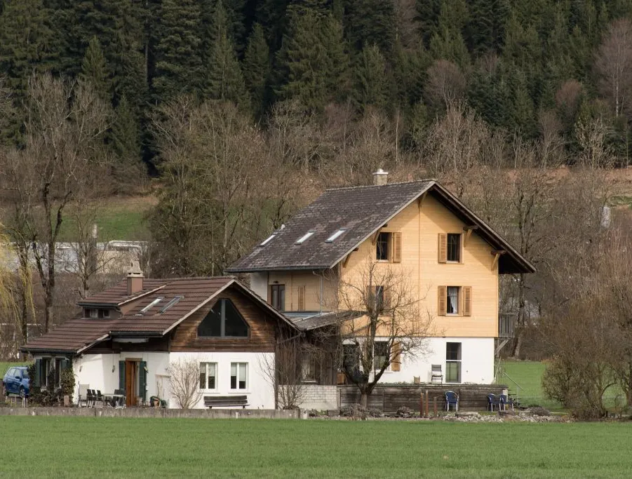 Referenzprojekt der Zimmerei Hirschi AG: Wohnhaus mit umfassend erneuerter Holzfassade, eingebettet in die typische Landschaft des Emmentals mit Wiesen und bewaldetem Hang.