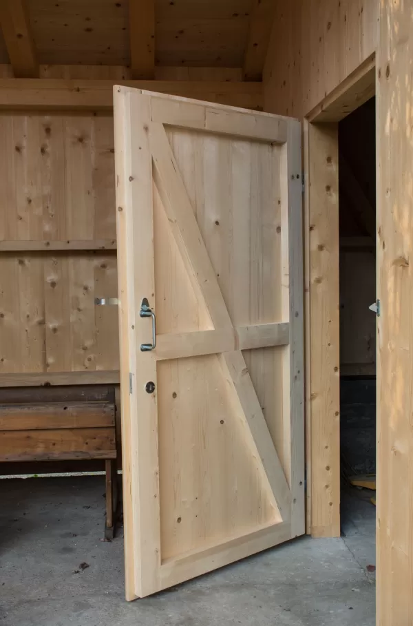 Geöffnete Holztür mit Metallgriff in einer Holzverkleidung, Blick in den dahinterliegenden Raum.