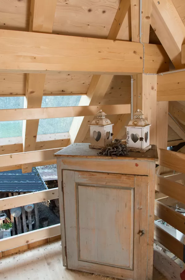 Dachraum mit sichtbarer Holzbalkenkonstruktion, altem Holzschrank und zwei dekorativen Laternen mit Herzmotiven.