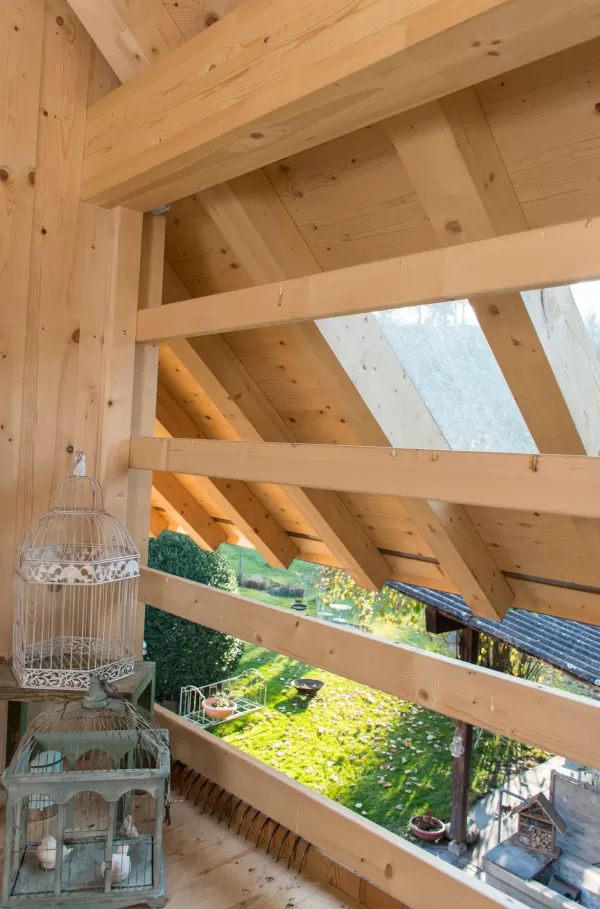 Holzbalkenkonstruktion mit Dachfenster und Blick ins Freie, dekoriert mit zwei Vogelkäfigen und Kerzen.