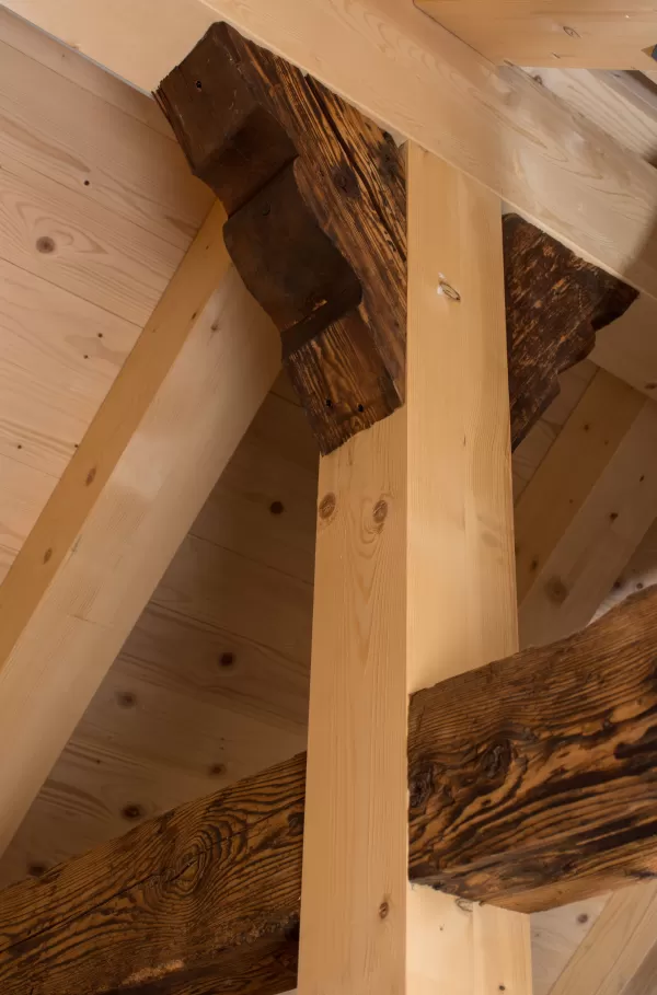 Detailaufnahme einer Holzbalkenkonstruktion mit sichtbaren alten und neuen Holzelementen im Dachbereich.