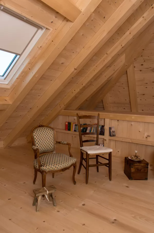 Gemütlicher Dachraum mit Holzboden, zwei Stühlen, kleinem Hocker und eingebautem Bücherregal unter der Schräge