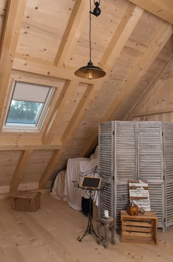 Dachzimmer mit Holzverkleidung, sichtbarer Balkenkonstruktion, Dachfenster und Raumteiler aus Holz, eingerichtet mit Notenständer und kleinen Möbeln