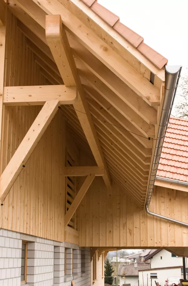 Detailansicht eines traditionellen Dachstuhls aus hellem Holz mit sichtbarer Balkenkonstruktion und Ziegeldach. Die präzise ausgeführte Zimmermannsarbeit zeigt stabile Verbindungen und eine saubere Verarbeitung.