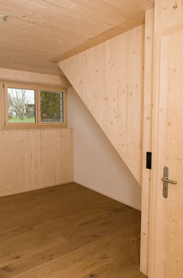 Gemütlicher Raum mit Holzdecke und Wandverkleidung aus Fichtenholz. Ein Fenster lässt Tageslicht herein und betont die natürliche Holzstruktur – ein harmonisches Zusammenspiel von Wärme und Schlichtheit.