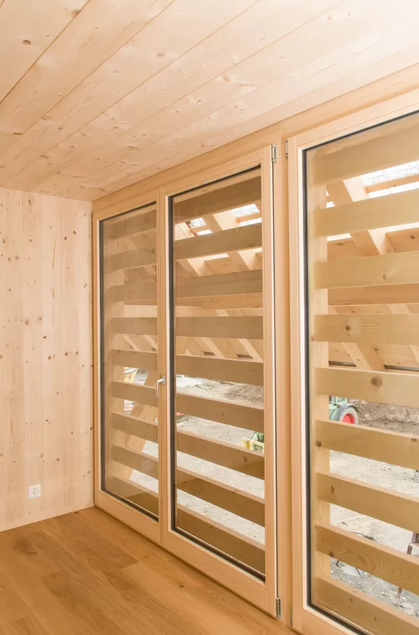 Heller Raum mit großflächiger Holzverglasung und horizontalen Lamellen. Die natürliche Holzstruktur an Wänden, Decke und Boden schafft ein warmes, einladendes Wohnambiente mit viel Tageslicht.