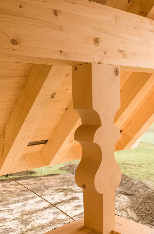 Detailaufnahme einer kunstvoll gearbeiteten Holzstütze unter einem Dachvorsprung. Die geschwungene Form und präzise Ausführung zeigen traditionelles Zimmermannshandwerk in hochwertiger Verarbeitung.