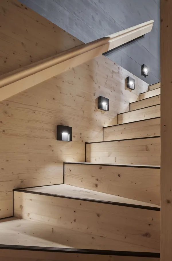 Traditionelles Holzhaus im Emmental in der Abenddämmerung, mit geschwungenem Giebeldach und aufwendig gestalteter Holzfassade. Warmes Licht fällt aus den Fenstern und betont die handwerklichen Details der historischen Holzkonstruktion. Das Gebäude steht in einer ruhigen, ländlichen Umgebung mit Garten, Bäumen und Holzzaun.