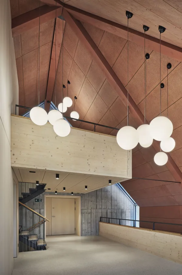 Traditionelles Holzhaus im Emmental in der Abenddämmerung, mit geschwungenem Giebeldach und aufwendig gestalteter Holzfassade. Warmes Licht fällt aus den Fenstern und betont die handwerklichen Details der historischen Holzkonstruktion. Das Gebäude steht in einer ruhigen, ländlichen Umgebung mit Garten, Bäumen und Holzzaun.