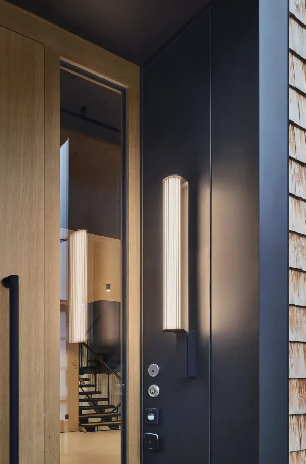 Traditionelles Holzhaus im Emmental in der Abenddämmerung, mit geschwungenem Giebeldach und aufwendig gestalteter Holzfassade. Warmes Licht fällt aus den Fenstern und betont die handwerklichen Details der historischen Holzkonstruktion. Das Gebäude steht in einer ruhigen, ländlichen Umgebung mit Garten, Bäumen und Holzzaun.