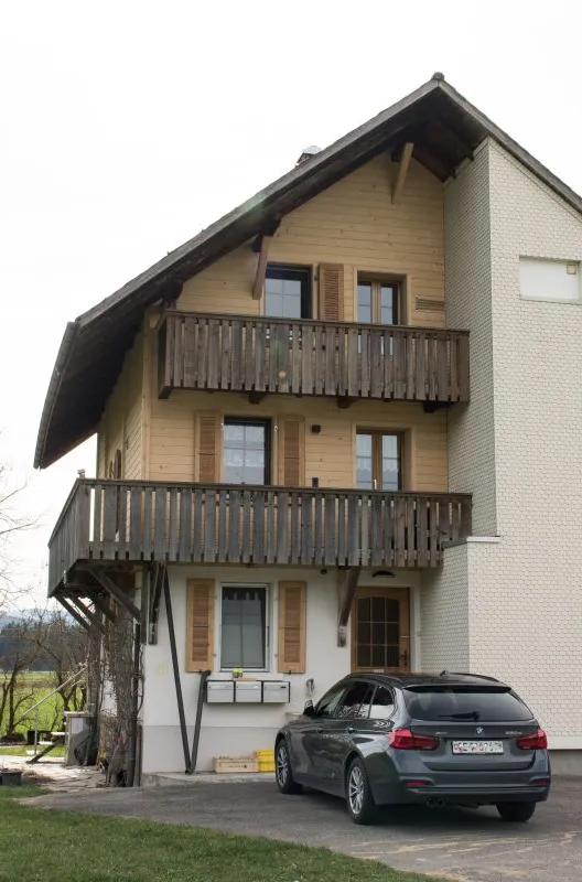 Referenzprojekt der Zimmerei Hirschi AG: Wohnhaus mit umfassend erneuerter Holzfassade, eingebettet in die typische Landschaft des Emmentals mit Wiesen und bewaldetem Hang.