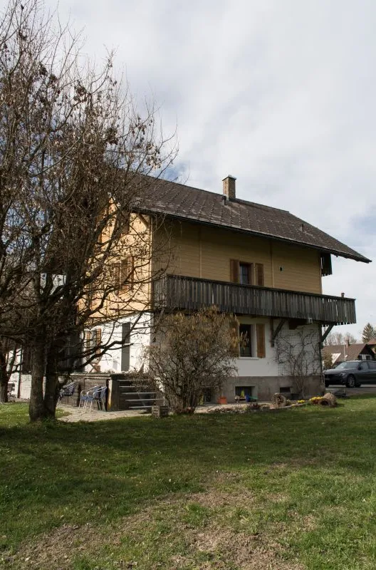 Referenzprojekt der Zimmerei Hirschi AG: Wohnhaus mit umfassend erneuerter Holzfassade, eingebettet in die typische Landschaft des Emmentals mit Wiesen und bewaldetem Hang.