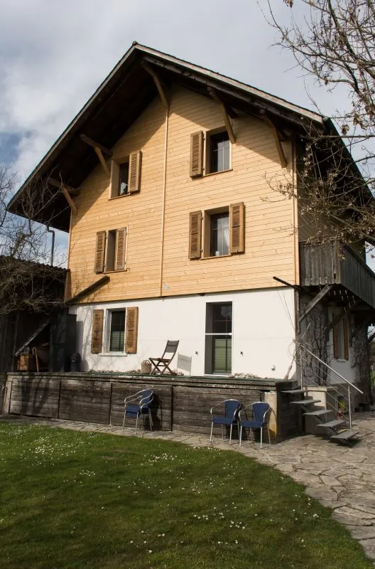 Referenzprojekt der Zimmerei Hirschi AG: Wohnhaus mit umfassend erneuerter Holzfassade, eingebettet in die typische Landschaft des Emmentals mit Wiesen und bewaldetem Hang.