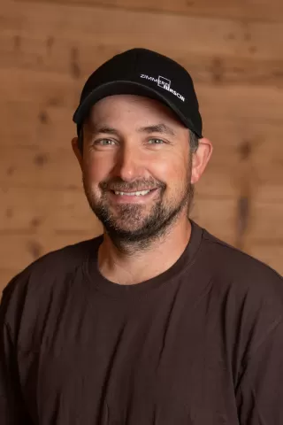 Mitarbeiterportrait / Foto mit braunem T-Shirt oder schwarzem Polo Shirt mit Zimmerei Hirschi Logo. Strahlend und lachend nach oben schauend oder direkt in die Kamera.