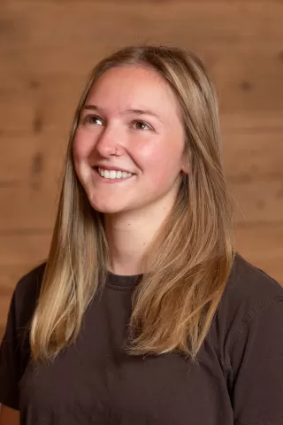 Mitarbeiterportrait / Foto mit braunem T-Shirt oder schwarzem Polo Shirt mit Zimmerei Hirschi Logo. Strahlend und lachend nach oben schauend oder direkt in die Kamera.