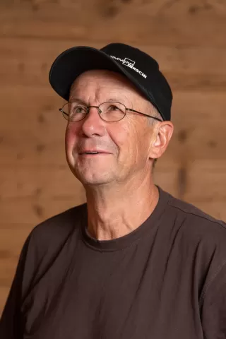 Mitarbeiterportrait / Foto mit braunem T-Shirt oder schwarzem Polo Shirt mit Zimmerei Hirschi Logo. Strahlend und lachend nach oben schauend oder direkt in die Kamera.