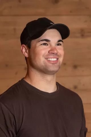 Mitarbeiterportrait / Foto mit braunem T-Shirt oder schwarzem Polo Shirt mit Zimmerei Hirschi Logo. Strahlend und lachend nach oben schauend oder direkt in die Kamera.