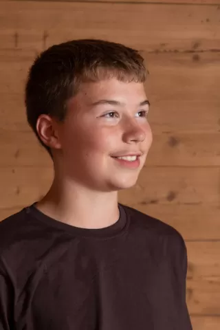 Profilfoto eines jungen Mannes mit kurzem, braunem Haar, der freundlich nach rechts blickt. Er trägt ein dunkelbraunes T-Shirt und steht vor einer natürlichen Holz-Wand.
