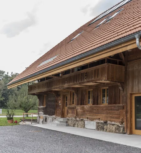 Gemütlicher Wohnbereich im Dachgeschoss mit sichtbaren Holzbalken, grauem Ecksofa und Holztisch.