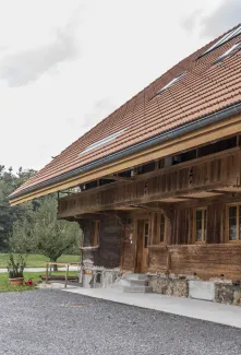 Gemütlicher Wohnbereich im Dachgeschoss mit sichtbaren Holzbalken, grauem Ecksofa und Holztisch.