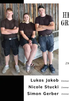 Für dieses Bild würde ich folgenden Alt-Text verwenden:  "Gratulationsplakat der Zimmerei Hirschi und Truberholz für drei erfolgreich abgeschlossene Lehrabschlüsse. Das Bild zeigt zwei junge Männer und eine junge Frau in Arbeitskleidung vor einer Holzfassade. Auf dem Plakat werden Lukas Jakob und Simon Gerber zum Abschluss als Zimmermann EFZ sowie Nicole Stucki zum Abschluss als Zimmerin EFZ beglückwünscht.