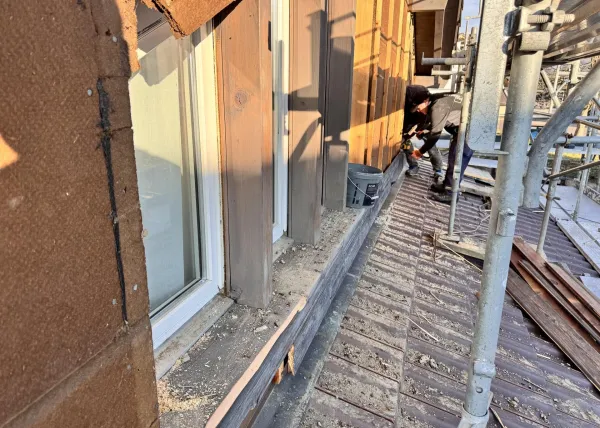 Holzhaus im Bau mit eingerüsteter Fassade und Baustellenbanner der Zimmerei Hirschi unter blauem Himmel.