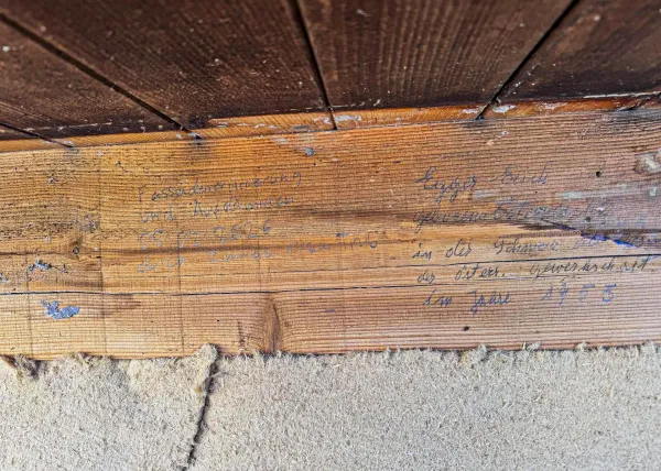 Holzhaus im Bau mit eingerüsteter Fassade und Baustellenbanner der Zimmerei Hirschi unter blauem Himmel.
