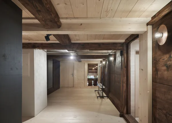 Traditionelles Holzhaus im Emmental in der Abenddämmerung, mit geschwungenem Giebeldach und aufwendig gestalteter Holzfassade. Warmes Licht fällt aus den Fenstern und betont die handwerklichen Details der historischen Holzkonstruktion. Das Gebäude steht in einer ruhigen, ländlichen Umgebung mit Garten, Bäumen und Holzzaun.