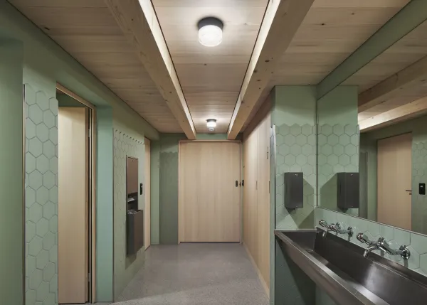 Traditionelles Holzhaus im Emmental in der Abenddämmerung, mit geschwungenem Giebeldach und aufwendig gestalteter Holzfassade. Warmes Licht fällt aus den Fenstern und betont die handwerklichen Details der historischen Holzkonstruktion. Das Gebäude steht in einer ruhigen, ländlichen Umgebung mit Garten, Bäumen und Holzzaun.