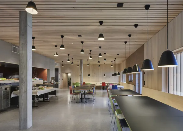 Traditionelles Holzhaus im Emmental in der Abenddämmerung, mit geschwungenem Giebeldach und aufwendig gestalteter Holzfassade. Warmes Licht fällt aus den Fenstern und betont die handwerklichen Details der historischen Holzkonstruktion. Das Gebäude steht in einer ruhigen, ländlichen Umgebung mit Garten, Bäumen und Holzzaun.