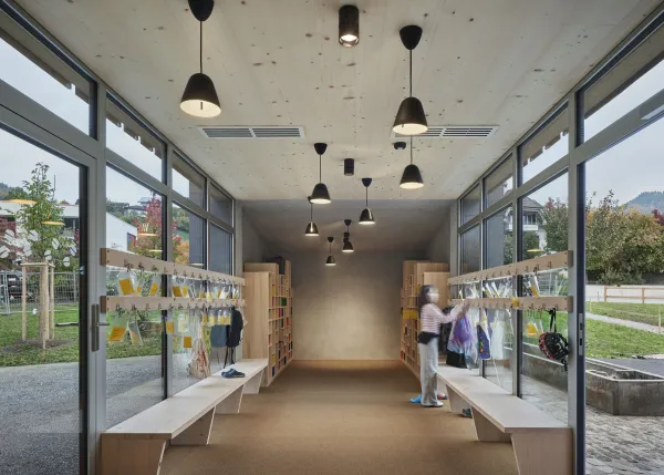 Traditionelles Holzhaus im Emmental in der Abenddämmerung, mit geschwungenem Giebeldach und aufwendig gestalteter Holzfassade. Warmes Licht fällt aus den Fenstern und betont die handwerklichen Details der historischen Holzkonstruktion. Das Gebäude steht in einer ruhigen, ländlichen Umgebung mit Garten, Bäumen und Holzzaun.