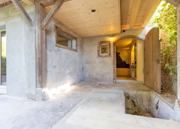 einblicke in ein holzbauprojekt in gunten: die aussenansicht zeigt ein haus mit heller holzfassade und balkon, eingebettet zwischen bäumen und einem steinmäuerchen. im inneren prägen helle holzdecken und sichtbare balken, grosse fenster und warme holzoberflächen die räume. zu sehen sind ein grosszügiger wohnbereich mit zugang zum balkon und ausblick ins grüne, eine holzküche mit arbeitsinsel sowie ein badezimmer mit rundem spiegel und aufgesetztem waschbecken. helles ziegelmauerwerk und sorgfältig erhaltene