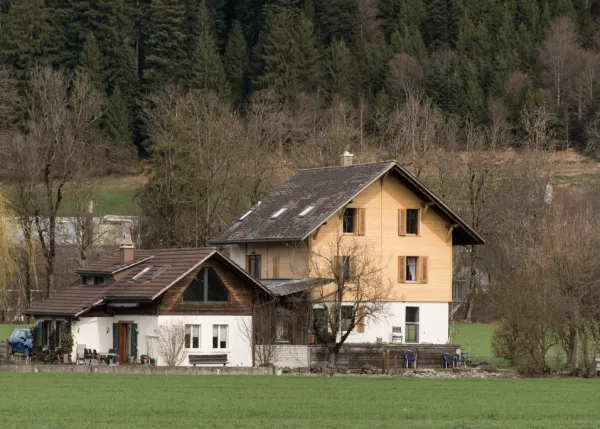 Referenzprojekt der Zimmerei Hirschi AG: Wohnhaus mit umfassend erneuerter Holzfassade, eingebettet in die typische Landschaft des Emmentals mit Wiesen und bewaldetem Hang.